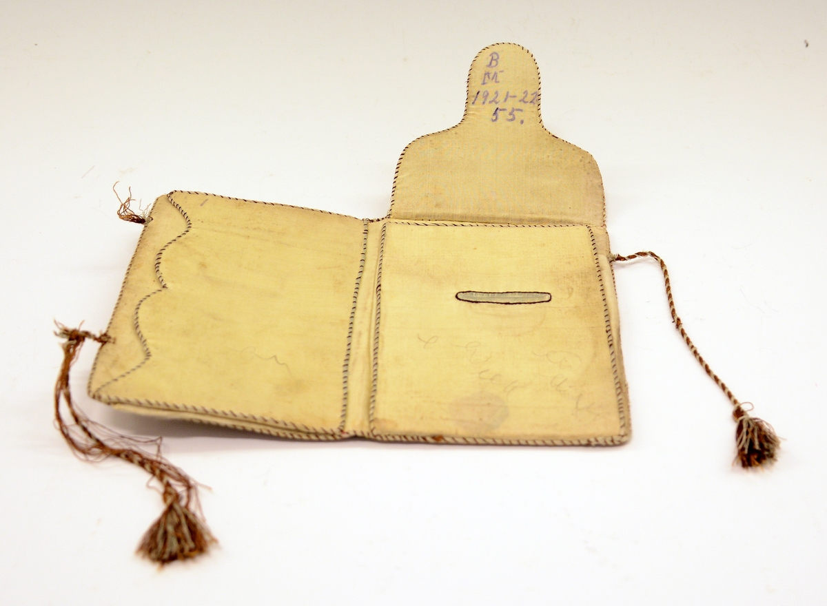 Lommebok i silke med brodert motiv og tekst. Innvendig med tre rom. Permane paaføra med gult og violet silkety med blomebrodering  paa utsidane. Paa framsida stend sauma: H.A. - Erkjendlighedsminde. Paa baksida eit tre, innaat dette eit ankar. Tvunnet silkeband.