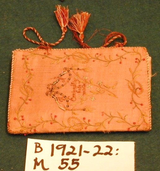 Lommebok i silke med brodert motiv og tekst. Innvendig med tre rom. Permane paaføra med gult og violet silkety med blomebrodering  paa utsidane. Paa framsida stend sauma: H.A. - Erkjendlighedsminde. Paa baksida eit tre, innaat dette eit ankar. Tvunnet silkeband.