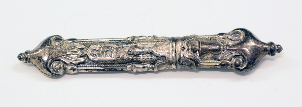 Nålehus i sølv. Drevet dekor, bl.a. med bjeller og våpenskjoldform med fugl og slange. 
Utydelig stempel: Ant. krone og (...)114.