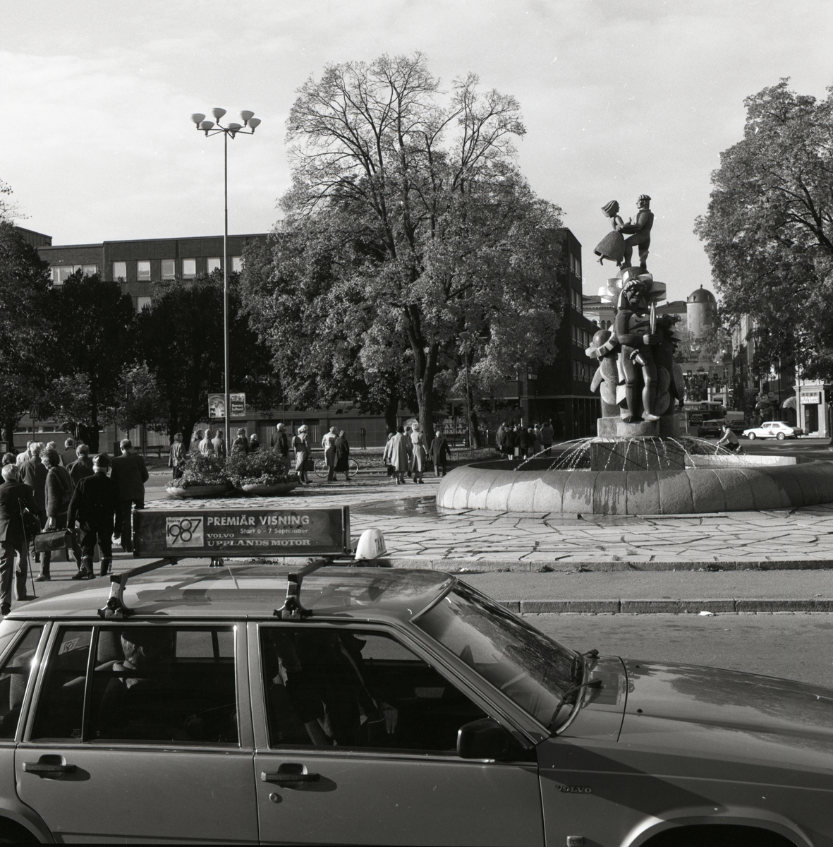 Bror Hjorths skulptur Näckens polska vid centralstationen i Uppsala 1986. Intill skulpturen går en grupp människor över torget.