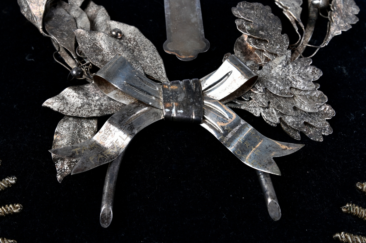 Sølvkrans av laurbær og eikeløv med sløyfe nederst. Mellom de bøyde greinene er det et sølvkors. Kransen er sydd ned på en svart fløyelspute med dusker i hjørnene. Sølvsnor påsydd rundt puta.

Det finnes to like kranser som denne publisert på Digitalt museum. Den ene er udatert, men den andre er også produsert i 1924 - og befinner seg på Mjøsmuseet.