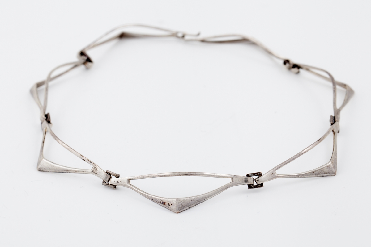 Halssmykke som består av sju ledd som er hektet sammen ved hjelp av små kvadrater. Hvert ledd har form som en halv rombe. "Diagonalen" nærmest halsen er en tynn sølvstreng. "Hjørnet" har en knekk. Fra dette smalner leddet mot yttersiden og ender i en krok. Disse hektes inn i det kvadratiske elementet. De ytterste leddene ender i en krok og et kvadrat som utgjør låsen.