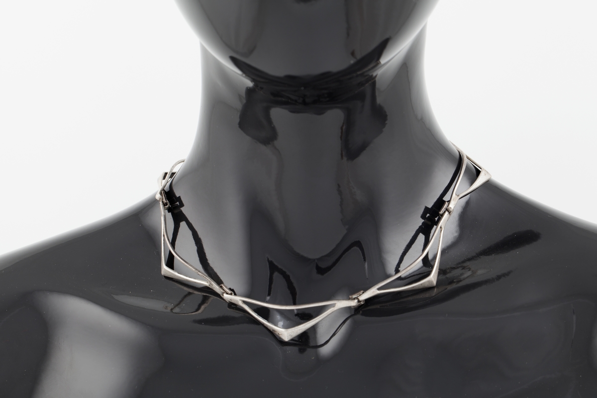 Halssmykke som består av sju ledd som er hektet sammen ved hjelp av små kvadrater. Hvert ledd har form som en halv rombe. "Diagonalen" nærmest halsen er en tynn sølvstreng. "Hjørnet" har en knekk. Fra dette smalner leddet mot yttersiden og ender i en krok. Disse hektes inn i det kvadratiske elementet. De ytterste leddene ender i en krok og et kvadrat som utgjør låsen.