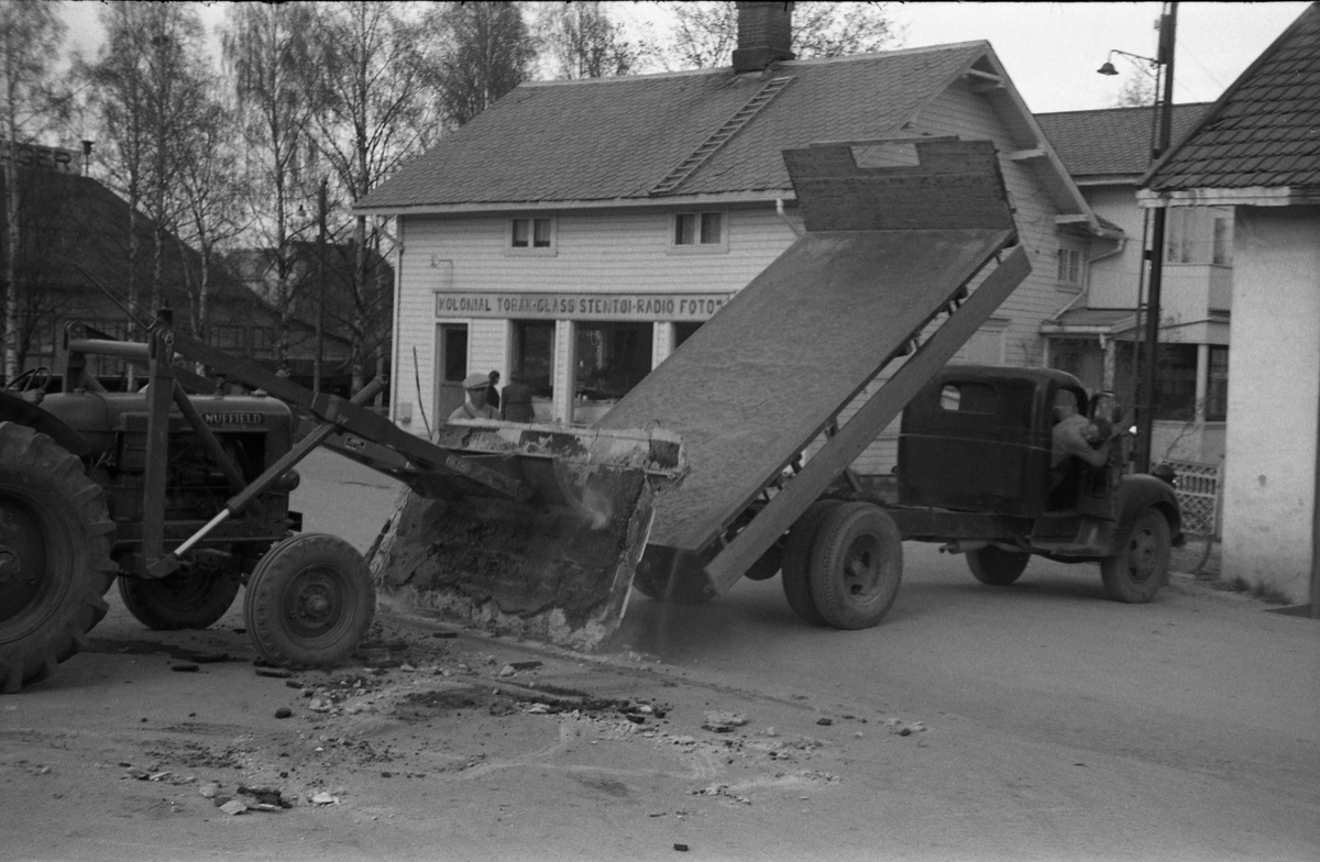 En lasteoperasjon i Lena sentrum april/mai 1954. Har trolig sammenheng med ombygging av Esso bensinstasjon, og det som man strever med å få opp på lastebilen er trolig noe fra rivingen. På bilde nr. fire kan en tydelig kjenne Paul Grindvoll med skyggelue, ellers er ingen av personene identifisert.