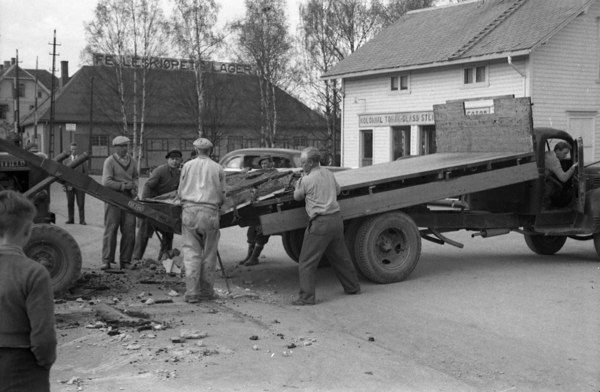 En lasteoperasjon i Lena sentrum april/mai 1954. Har trolig sammenheng med ombygging av Esso bensinstasjon, og det som man strever med å få opp på lastebilen er trolig noe fra rivingen. På bilde nr. fire kan en tydelig kjenne Paul Grindvoll med skyggelue, ellers er ingen av personene identifisert.