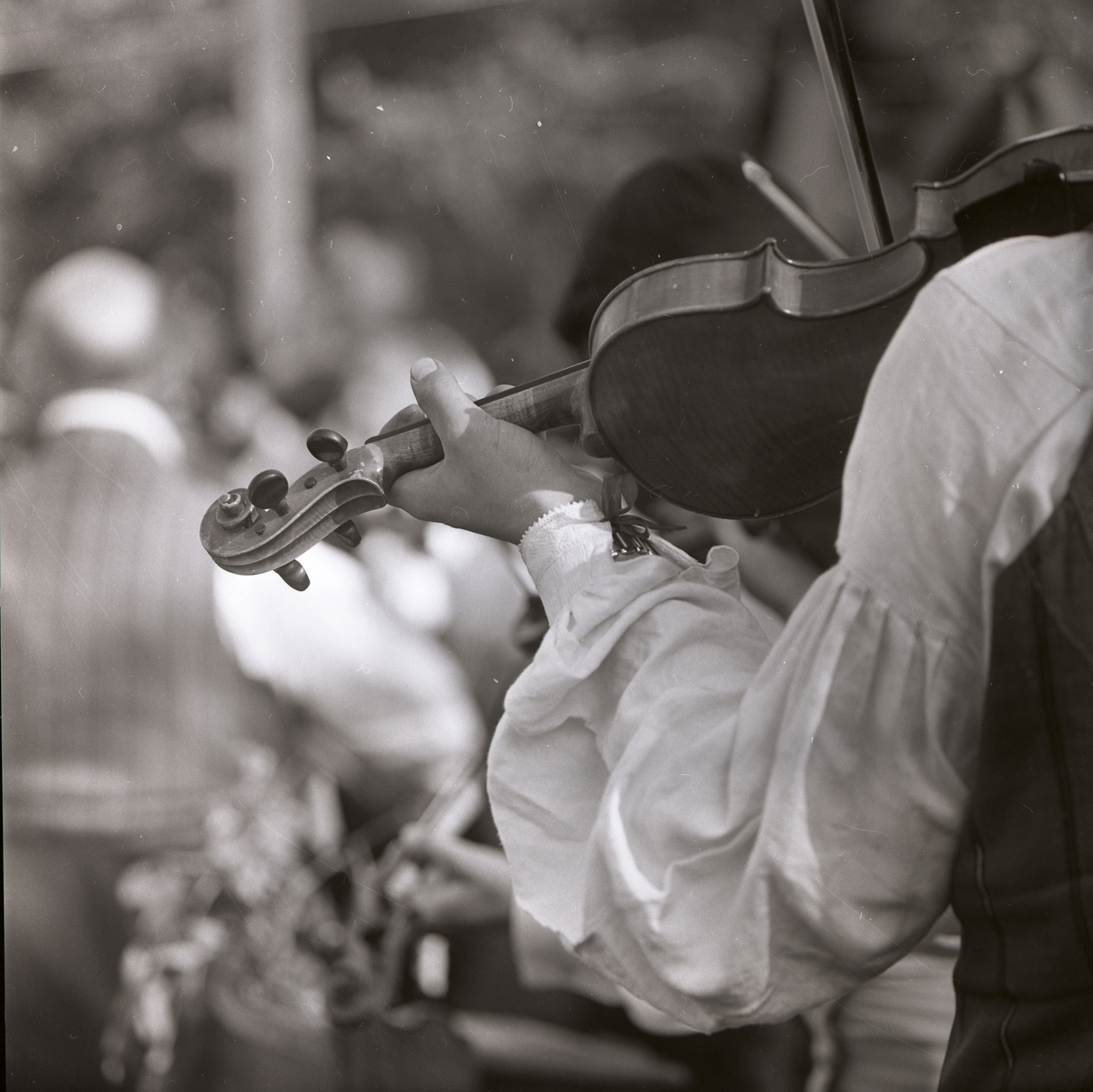 En spelman syns spela på en fiol vid hembygdsgården i Rengsjö, 7 juni 1983. Endast hans ena arm syns på bilden.