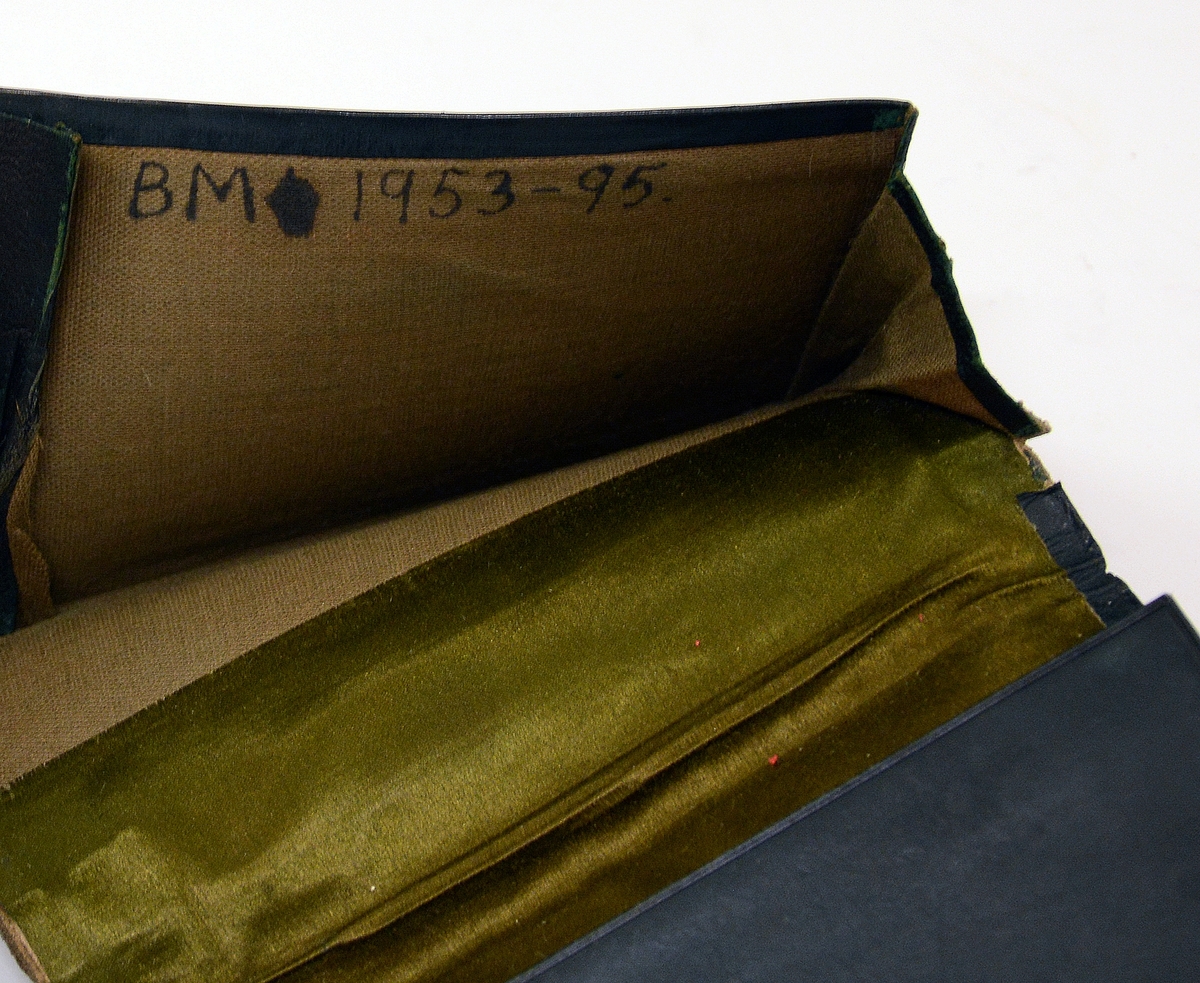 Liten lommebok i grønt skinn med to rom, mosegrønt fôr. Utsiden med preget dekorrender i gull. En side mangler sømmen.
Innlagt konvolutt med to resepter fra Henrik Ibsens privatlege, Dr. med. Edvard Bull. Den ene resepten datert 14/3 1903. En tredje resept, italiensk, datert 31. mai 1897.