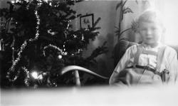 Barn ved siden av juletre i stue.