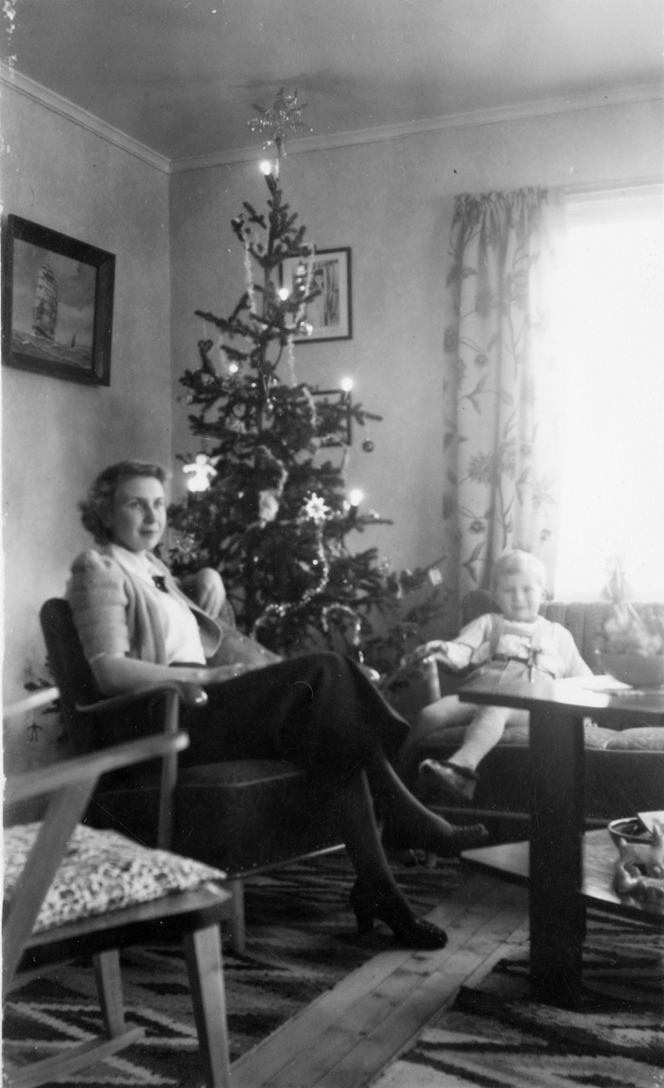 Kvinne med barn sittende i stue ved juletre.