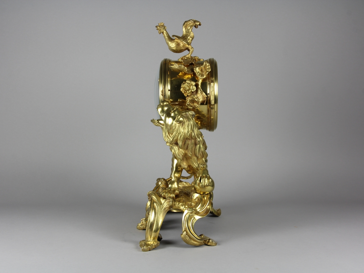 Urhuset i form av en tunna som står på ett rytande lejon med ena foten på ett klot på ett genombrutet rocailleornament. Ovanpå tunnan står en galande tupp, på sidorna rosor och växter.