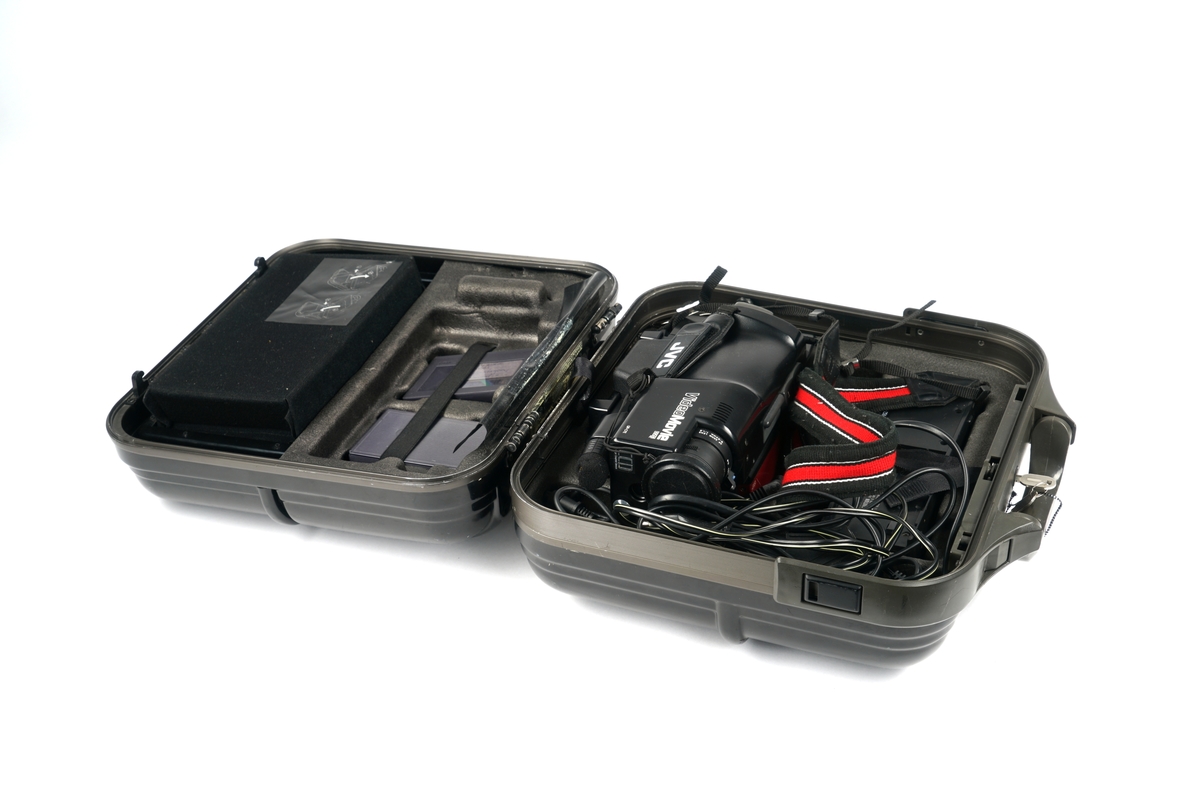 Videokamera med bæresele og med okkular og linse samt diverse funksjonstaster . Luke på siden for isetting av videokasett. En kasett sitter i kameraet. Kameraet ligger i en låsbar ( to nøkler medfølger) plastkoffert sammen med  tre ulike funksjonskabler sammen med et strømadapter. I kofferten er det et eget rom for et kassettadapter som igjen ligger i et etui. I adapteret ligger det en kassett. Videre medfølger det et tomt kassettetui samt ett etui inneholdene en kassett.