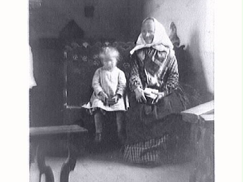 "Med mormor till kyrkan år 1890"
E5804_1: Gammal kvinna står utomhus med ett litet barn vid ena handen och en tjock bok i den andra, troligen en bibel då de på bild nr 2 sitter i Tjärby kyrka.
E5804_2: Gammal kvinna och litet barn sitter på en utsirad bänk i Tjärby kyrkas kor. Man ser lite av altartavlan och altarringen.