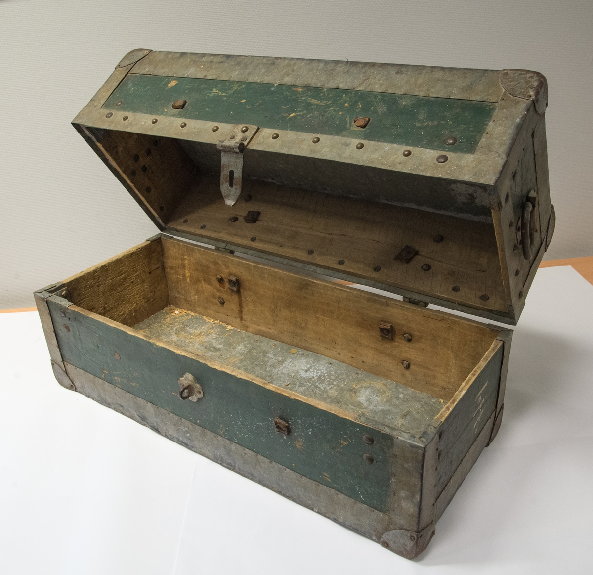 Rektangulær kiste av tre med hengsla lokk. Lik høgd på lokk og botn. Beslag for hengelås. Handtak i sidene for transport. Forsterka med kraftige metallvinklar i hjørnene innvendig. Kledd med metallplate på topp / lokk utvendig. Forsterka med metall i dei fleste kantar/hjørner. Metallband langs lanten av lokket er nagla fast. Inni er det spor etter kraftige skinnreimar som har vore nagla fast, men som no er kappa.
