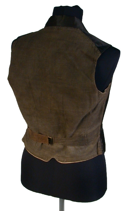 Med framstycke av svart siden, ryggstycke av svart domestik. Sleifar i ryggen med mässingsspänne. Foder av vit lärft. Dubbelknäppt, med 4 stycken svarta knappar i varje rad, på västens innersida en knapp med profilhuvud.