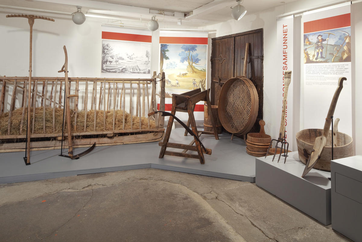 Bildet viser gjenstander i utstillingen. Det er en høybinge, ljå og kornsil.