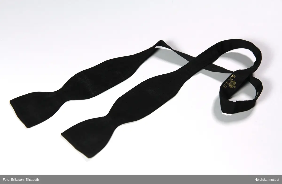 Halsduk, för herre, för smoking. 1940-tal
Av svart sidenrips, rosett att knyta. Firmamärke: 'MEA militärekiperings A/B Stockholm'.
Har tillhört upptäcktsresande författaren fil. dr Sven Hedin.