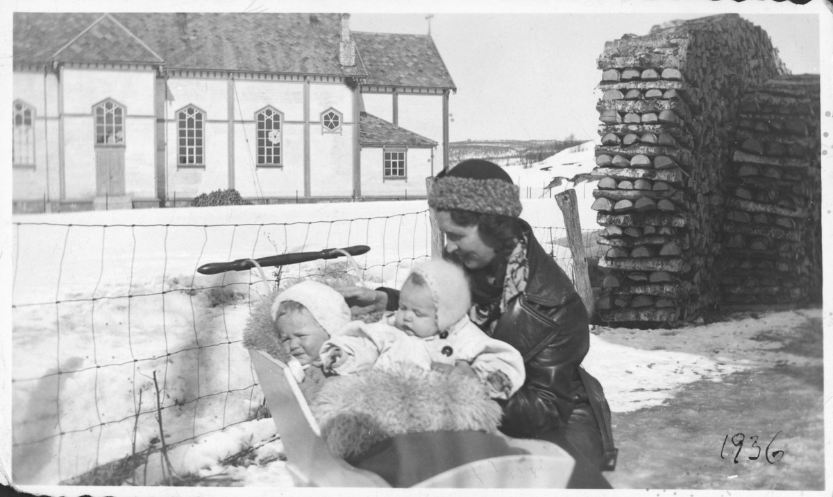 Kvinne med to barn i ei vogn. Skånland kirke i bakgrunnen.