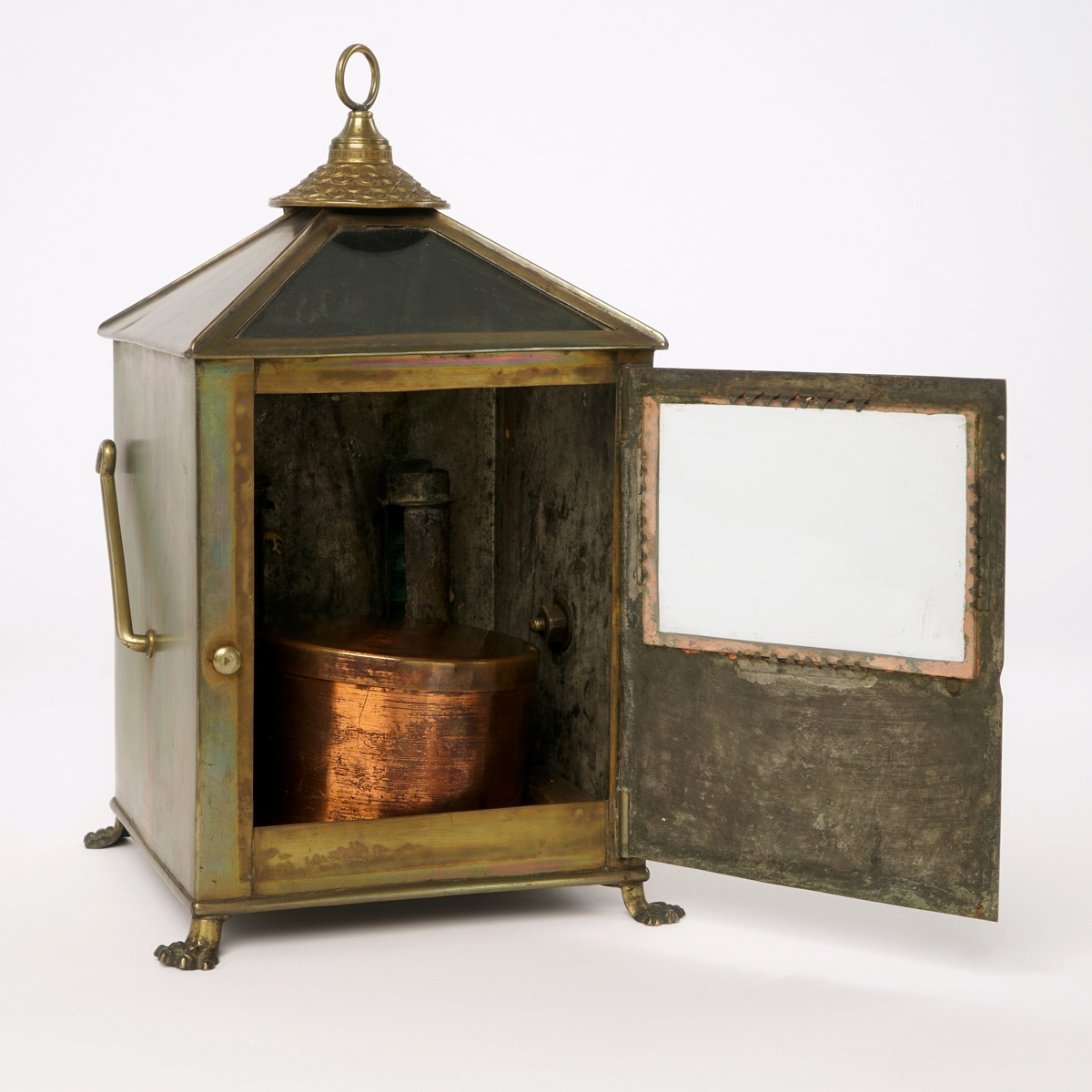 Firkantet kompasshus av metall med dør med vindu av glass. Døren kan låses med krok. Fire forsirede føtter av metall.  Tak som skråner til alle fire sider med vindu på takets forside. Luftavtrekk. Toppen av taket er utstyrt med forsiret deksel med bærering. To støttekroker, èn på hver side. Inne i huset er det to stearinlysholdere med metallfjær-innretning. Mellom disse er det fastmontert et metallrør.
Videre medfølger det to støtteklosser av tre for kompasset. Kompasslokk følger også med.