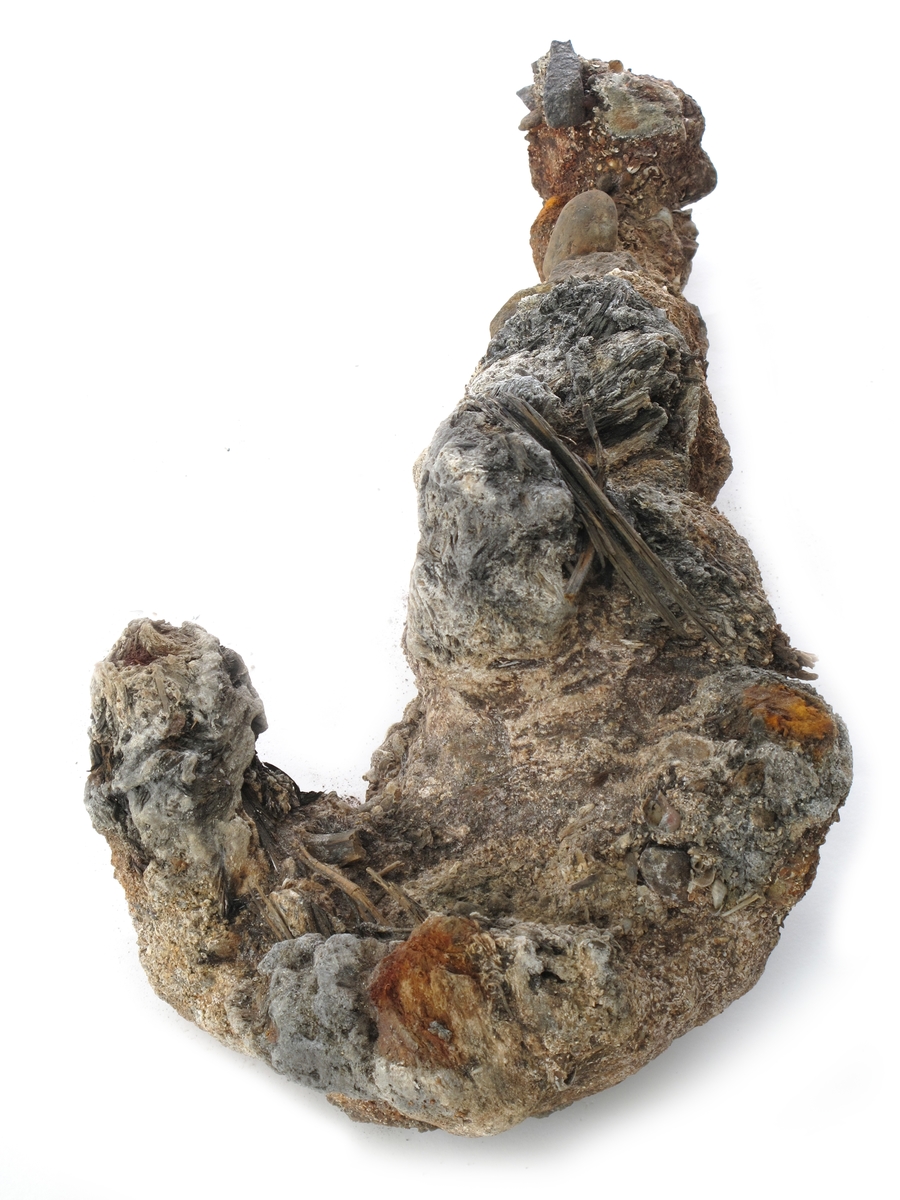 Korrosjonklump e) 
Korrosjonsklump omkring et stykke jern. Består av jern, rust, stein, sand og rester av treverk.