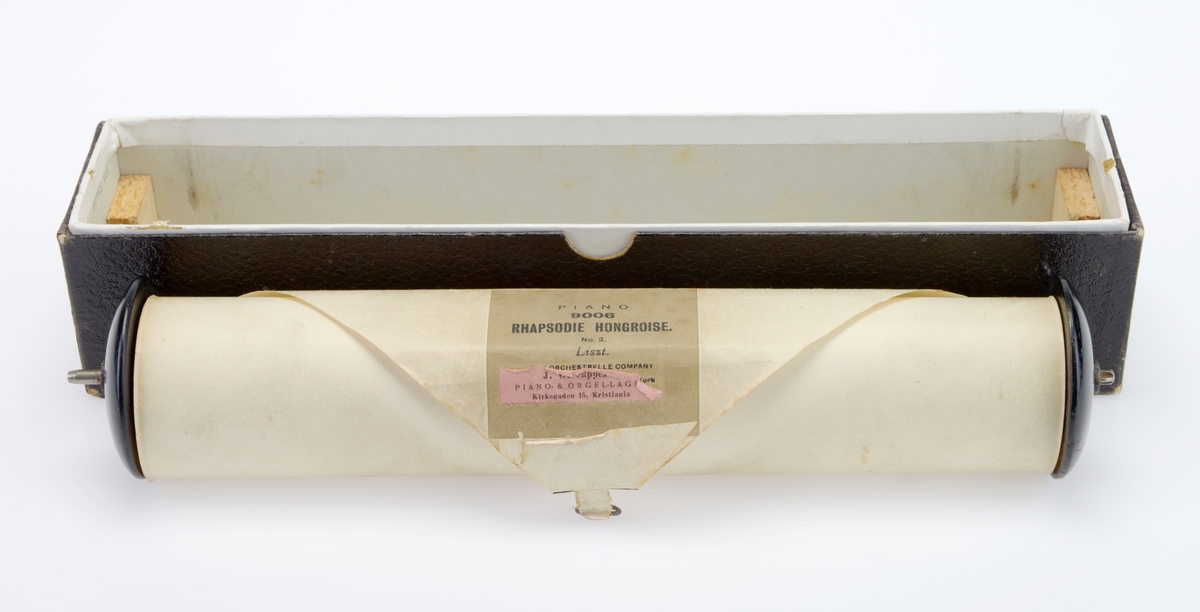Rull til selvspillende piano med tilhørende eske. Musikkrullen er av hvitt papir og er rullet opp på en spole av tre der endestykkene er malt svart. I hver side er det metallfester for innsetting i selvspillende piano. På den første delen av rullen er det limt på en etikett med informasjon om musikkstykket. Etiketten er grå med svart skrift. På denne etiketten er det limt på en mindre rosa etikett med informasjon om forhandleren. Deretter er det trykt/stemplet informasjon om patent i Storbritannia, USA og Frankrike. I enden er det limt på en hvit tekstilbit. I denne er det festet en liten metallring. Esken er laget av papp og er i to deler, esken er trukket med hvitt papir mens lokket er trukket med brunt papir.  Papiret på lokket har blindpreg. Foran på esken er det en brun etikett med påtrykt tekst med informasjon om musikkrullen, se "Påført tekst/merker".  Nede i esken er det limt fast en trekloss med hakk i hver ende, dette for at rullen skal ligge stødig i esken.