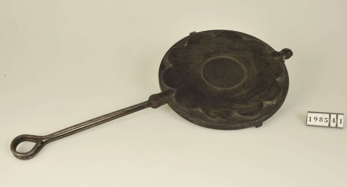 Fem hjärtformade delar. Handtag av rundjärn. Plansvarvad
botten.
Märkt: HUQVARNA NR 10 NORRAHAMMAR.

Persondata: Blenda Lysén  og. Jacobsson, Hjärtum sn.
B.L. gift på 1920-t. med kusinen Werner Lysén, Ytterby, Lundby frs.

Flyttade till Härröd, lärarbostaden, Lundby frs.
B.L. var hemmafru och fick 5-6 barn.

Anna Olausson fick våffeljärnet i vängåva f. 1933.
A.O. bodde då i Färjenäs, Lundby frs., 1934-1938.

V. L. skollärare fr. Ytterby, Lundby frs.

A.O. berättar att det var högst ovanligt att äta våfflor:: då man
gjorde det var det med blåbärssylt till.
