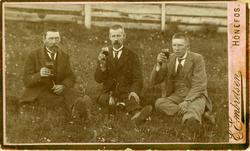 Tre menn sitter i gresset og skåler. Fra venstre Kristian An