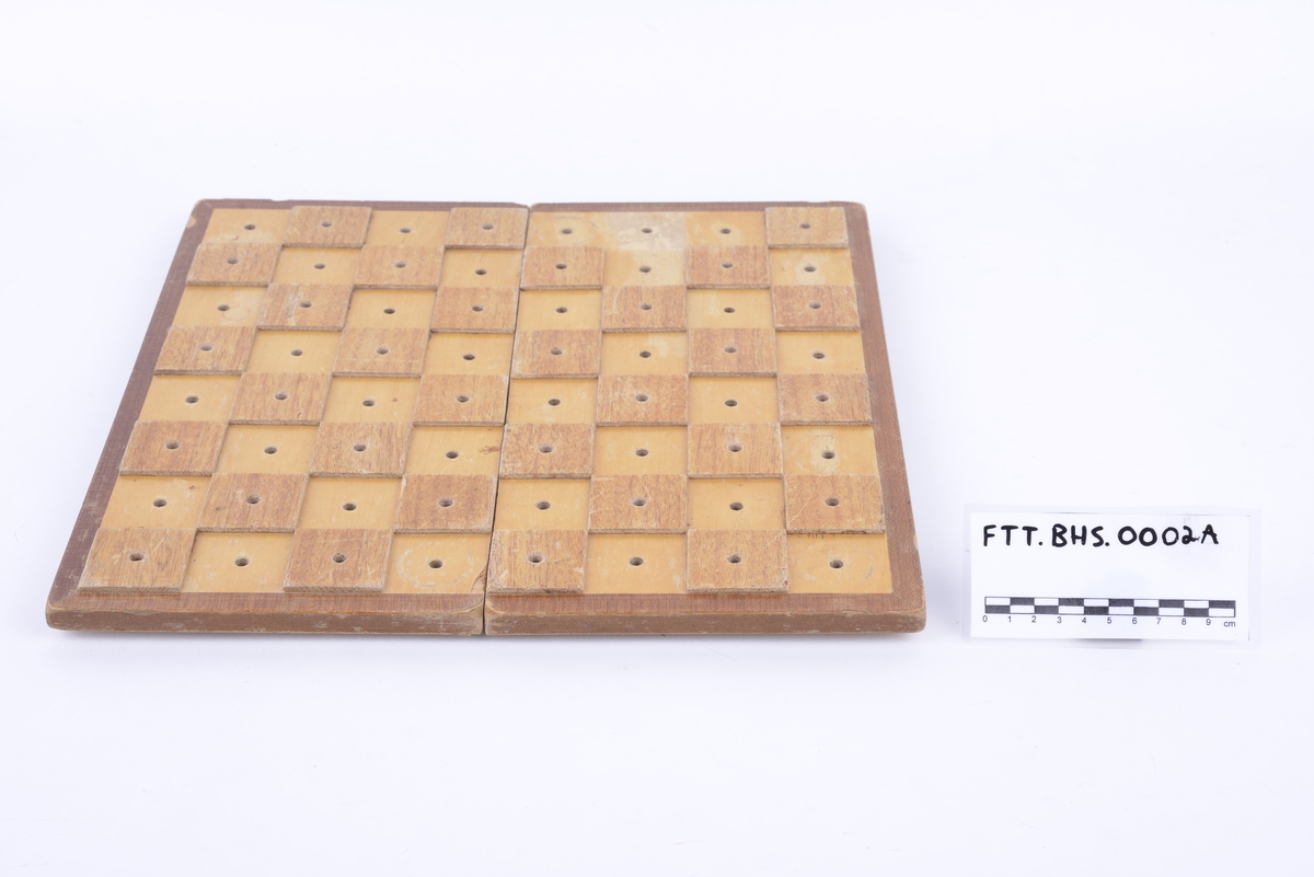 Sammenleggbar hengslet kasse i lakkert tre med brettspill på utsiden. Har tilhørende spillebrikker som ligger i en plastkrukke. 16 svarte og 16 i lakkert tre. Brikkene har pigger som kan stikkes ned i hull i brettet.