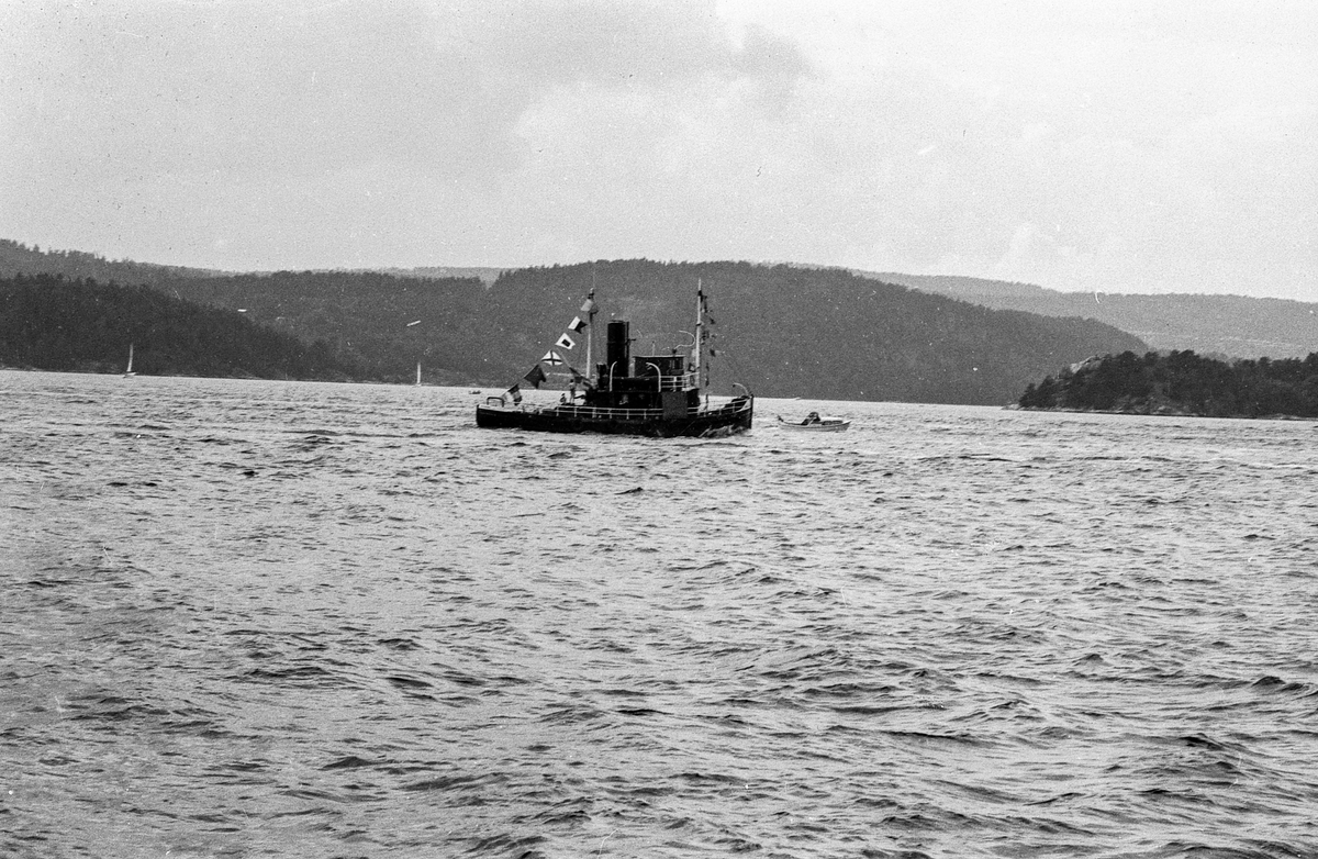 Drøbaksfjorden, sundet ved Oscarsborg. Tre menn på brygga ser på båtene med kikkert. Sandtaket og småhus på Hurum.
Fotograf: ØB Rønning
