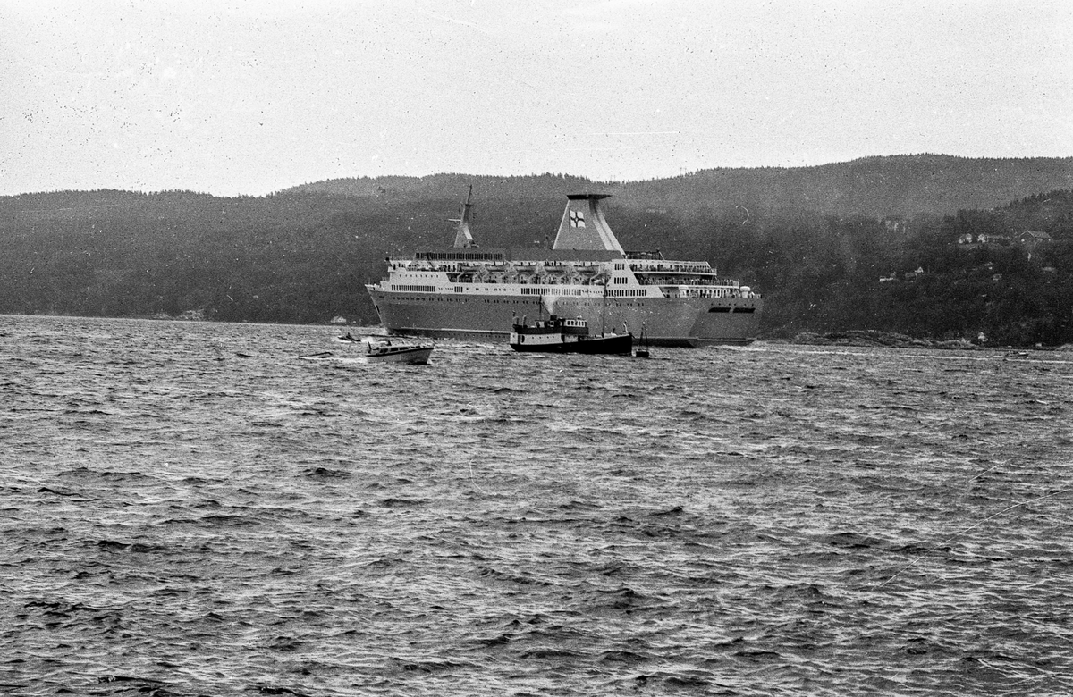 Drøbaksfjorden, sundet ved Oscarsborg. Tre menn på brygga ser på båtene med kikkert. Sandtaket og småhus på Hurum.
Fotograf: ØB Rønning