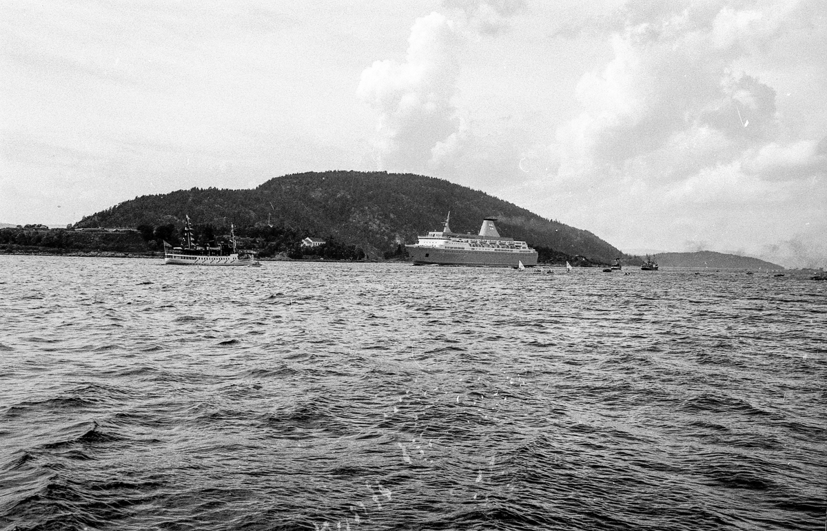 Drøbaksfjorden, sundet ved Oscarsborg. Tre menn på brygga ser på båtene med kikkert. Sandtaket og småhus på Hurum.
Fotograf: ØB Rønning