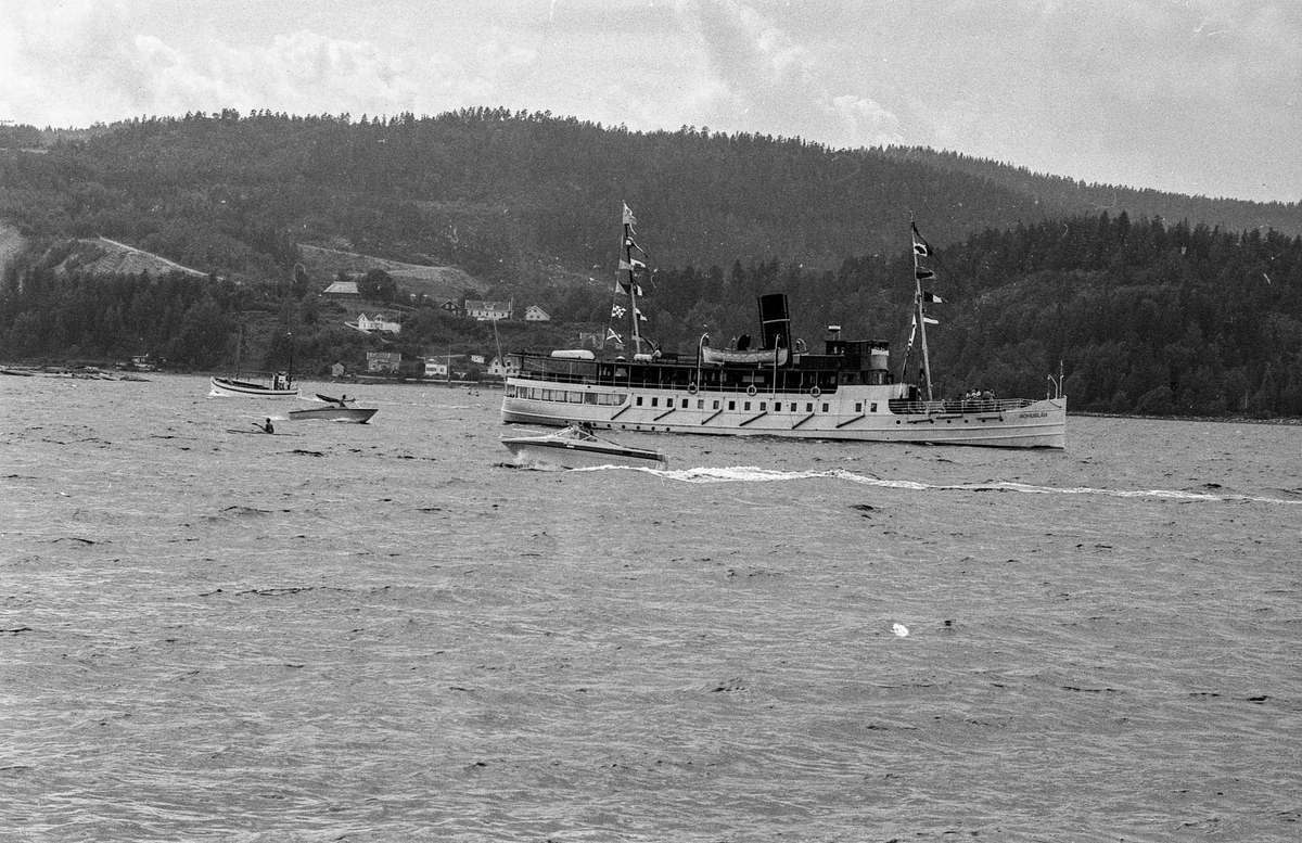 Drøbaksfjorden, sundet ved Oscarsborg. Tre menn på brygga ser på båtene med kikkert. Sandtaket og småhus på Hurum.
Fotograf: ØB Rønning