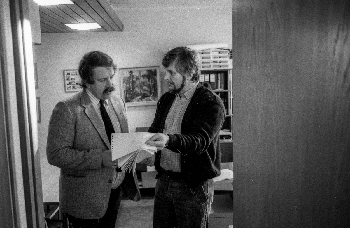 Ås trygdekontor stenger som en aksjon for å få utbedret dataanlegget som de er helt avhengige av. Salgsjef Olav Dalåsen i Norsk Data i samtale med trygdesjef Jan Espeland står i døråpningen med papirer.