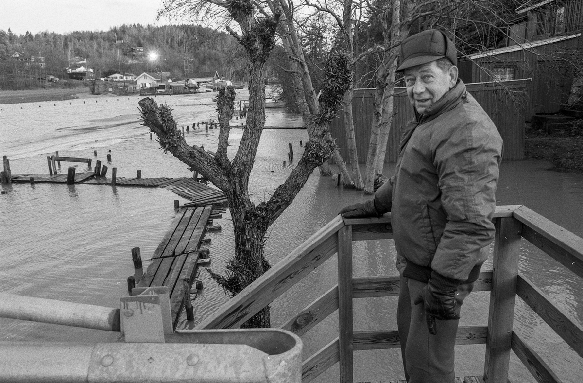 Flom ved marinaen i Son. Sjøen går opp til brygga og over trapper og gjerder. Tre menn ser på. Karlsen, Jacobsen og Hansen.
