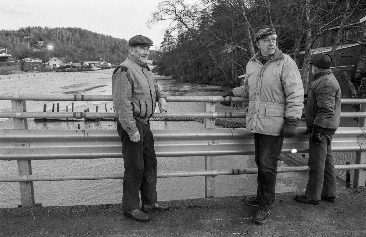 Flom ved marinaen i Son. Sjøen går opp til brygga og over trapper og gjerder. Tre menn ser på. Karlsen, Jacobsen og Hansen.