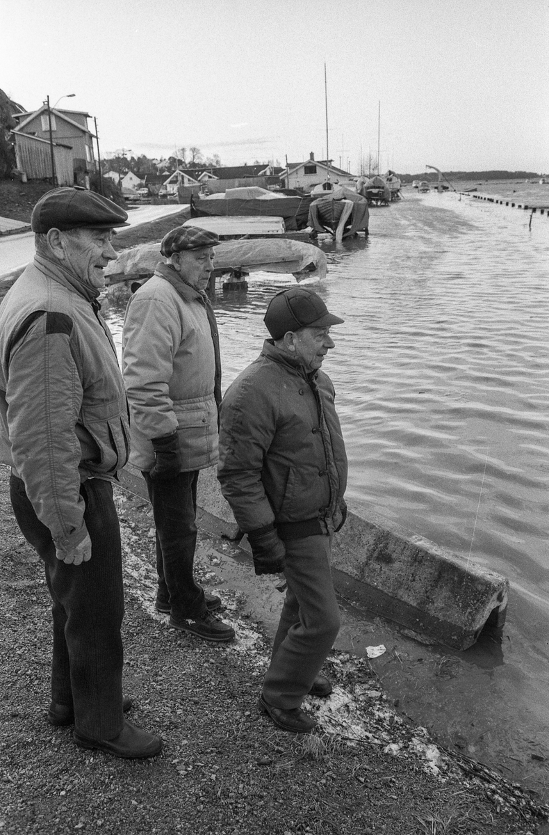 Flom ved marinaen i Son. Sjøen går opp til brygga og over trapper og gjerder. Tre menn ser på. Karlsen, Jacobsen og Hansen.