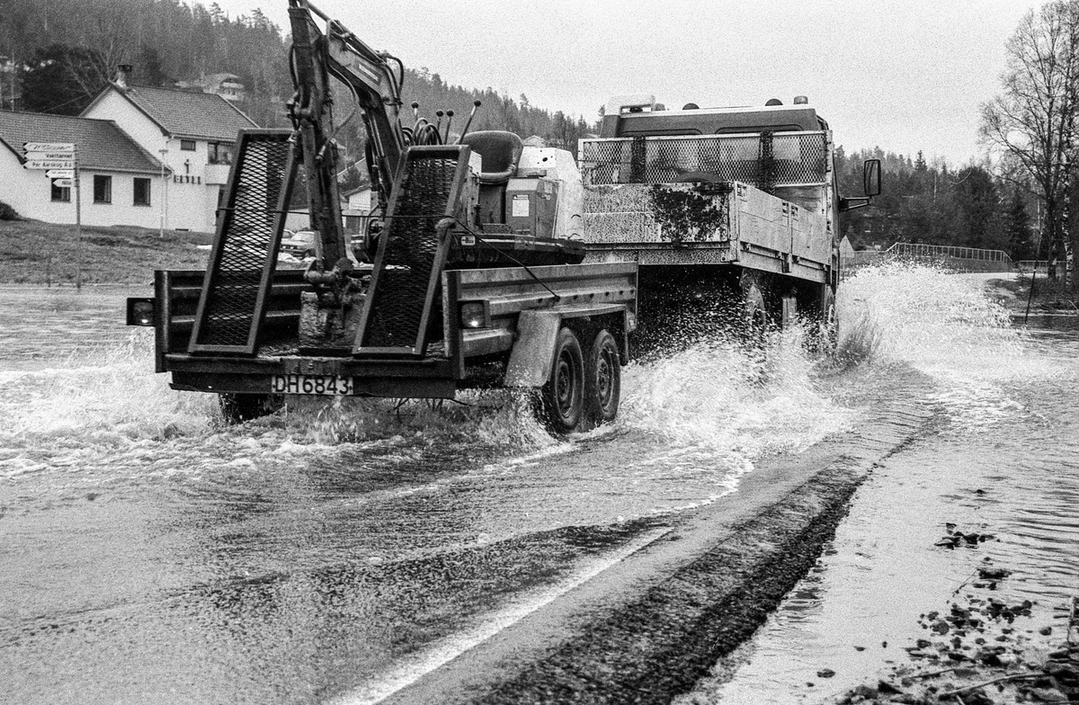 Flomskader på veiene, Riksvei 120, Ytre Enebakk. Vannet flommer over veier og jorder, biler kjører så vannspruten står.