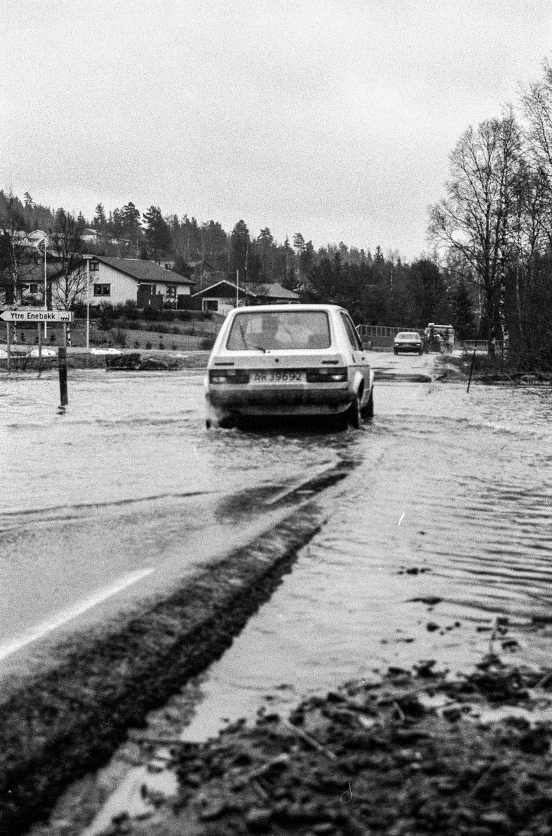 Flomskader på veiene, Riksvei 120, Ytre Enebakk. Vannet flommer over veier og jorder, biler kjører så vannspruten står.