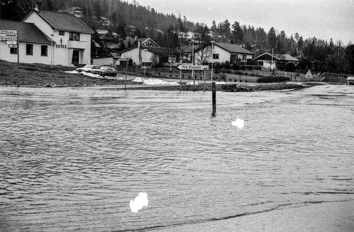 Flomskader på veiene, Riksvei 120, Ytre Enebakk. Vannet flommer over veier og jorder, biler kjører så vannspruten står.