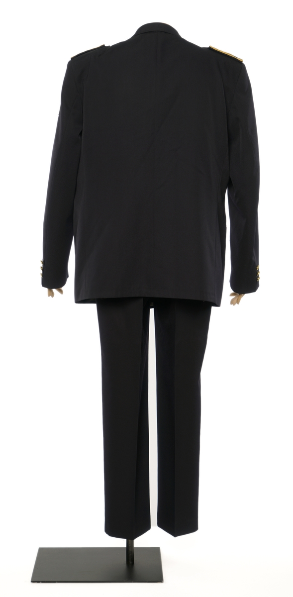 Mørkblå jakke enkelspent med tre riksløveknapper. Epauletter distinktsjoner, tre eikeblade med gullbånd. Tekstil marke på venstre arm, riksløve med hvit øks omgitt av eikeblader over TOLL. Hempe i nakke. Kypert stoff, blanding av polyester og ull. Jakke er foda med antatt syntetisk stoff, sort.
Bukser av samme stoff.