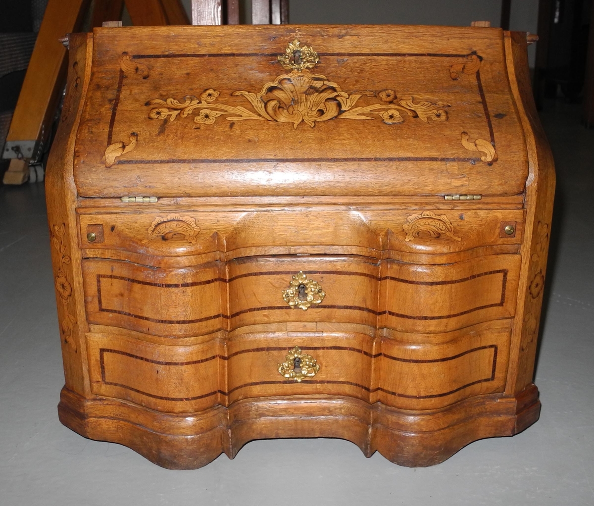 Barneskatoll i rokokkostil med separat overskap og underskap samt felles nøkkel til begge deler. Underskap med kraftig buet og profilert front, to skuffer samt nedfellbart pultlokk med hylle-, skap- og skuffseksjon innenfor. Overskap med to rette dører og kraftig profilert, delvis gjennombrutt gesims. Både over- og underskapet rikt dekorert med intarsia av høy kvalitet med rocailler, skjell, konturlinjer og blomsterornamentikk. Dekorative skilt av messing rundt alle nøkkelhull. Initialer og årstall på skapdør bak pultlokk. Skatollet står på to lave føtter.

A: underskap
B: nøkkel
C: overskap