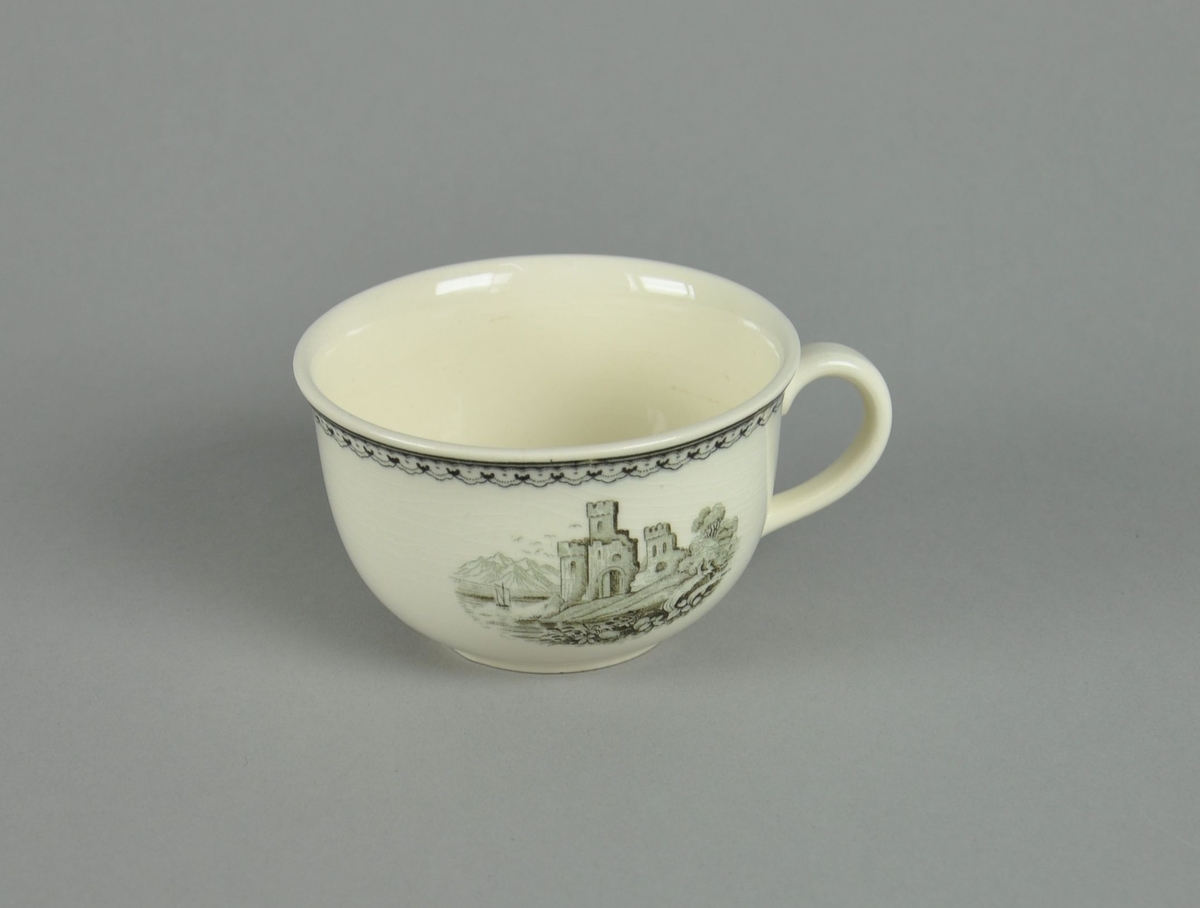 Kopp av glassert keramikk, med hank. Svart dekortrykk av klosterruiner og gård, samt en borde langs randen.