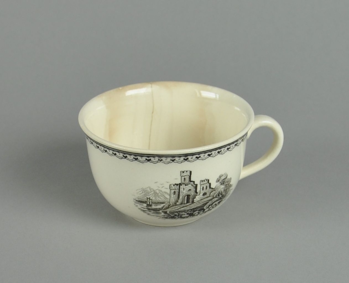 Kopp av glassert keramikk, med hank. Svart dekortrykk av klosterruiner og gård, samt en borde langs randen. Koppen har en synlig sprekk.