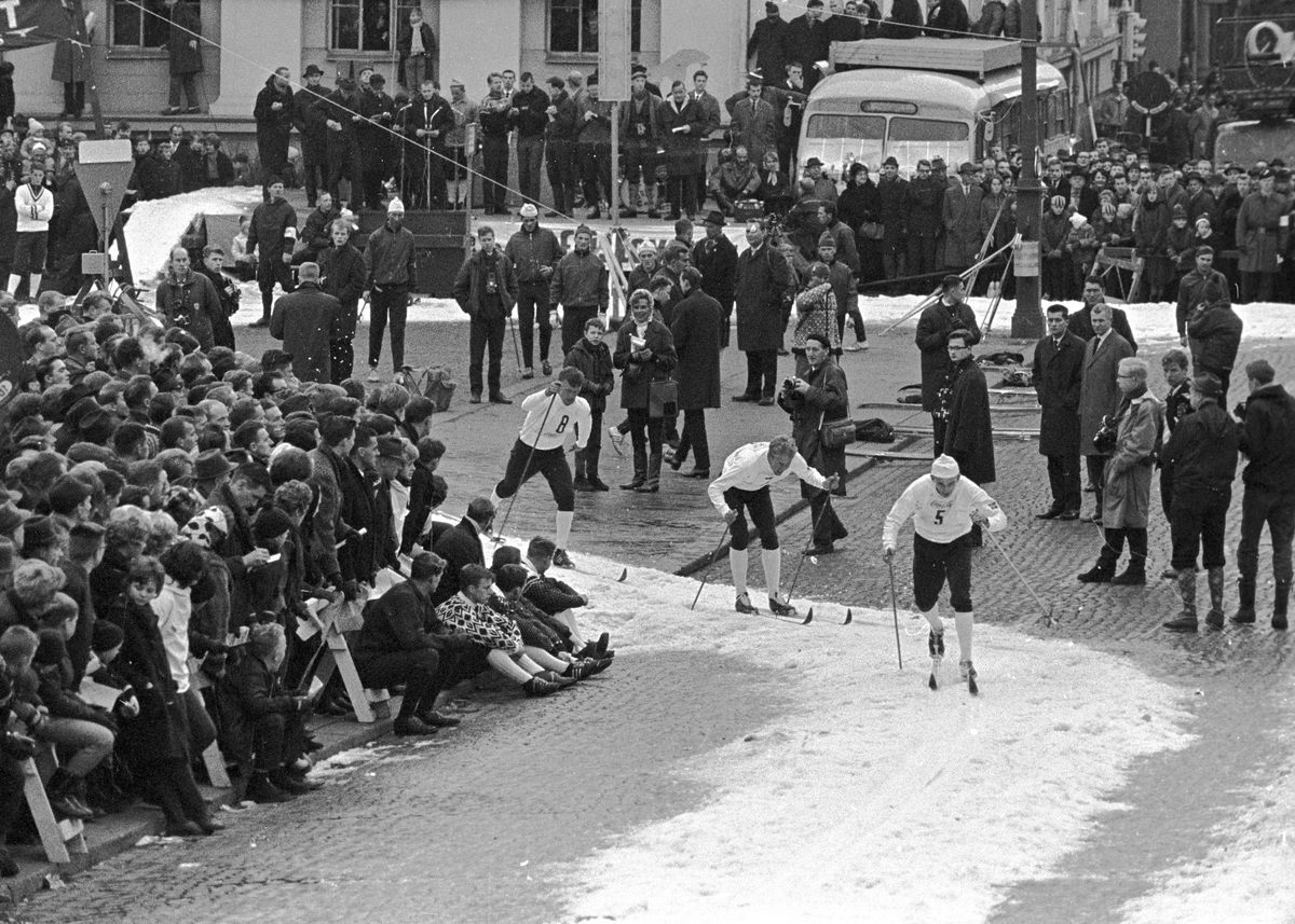 Mange skiløpere går forbi tilskuere og pressefolk som står langs løypa opp mot slottet, Slottsrennet. Fotografert november 1964.