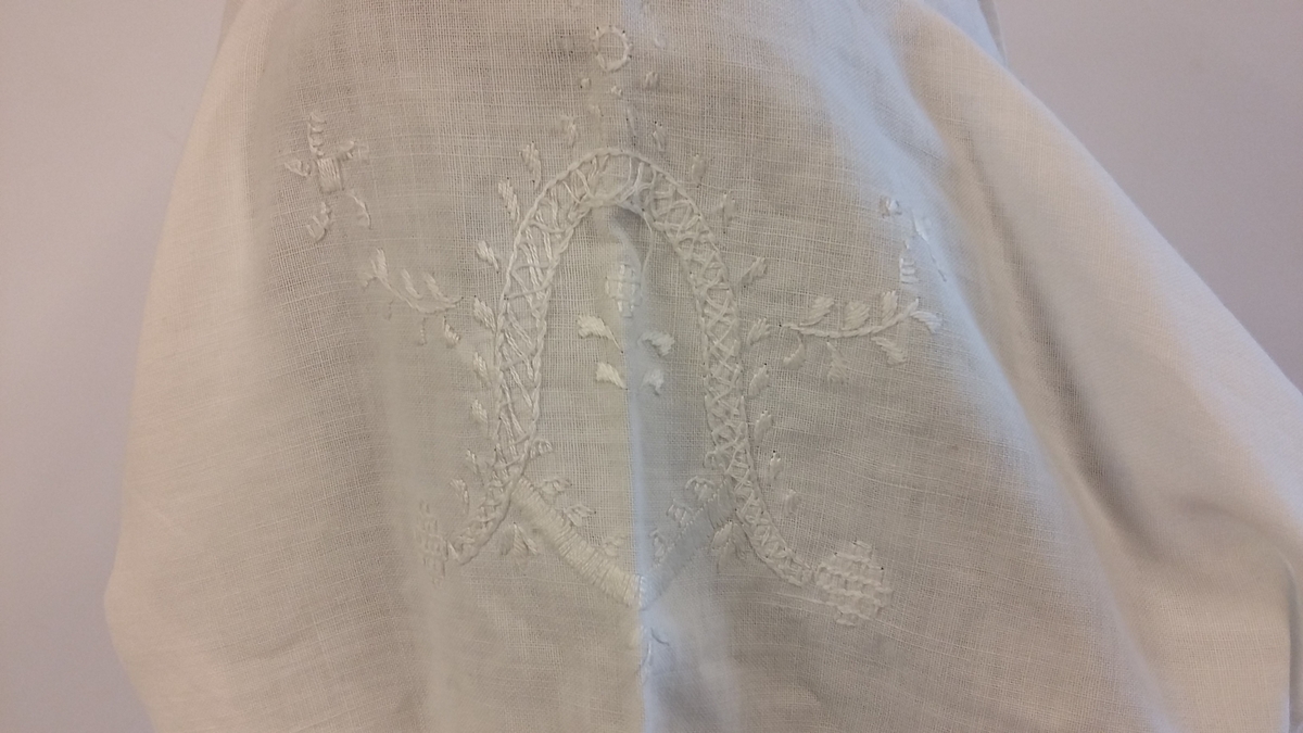 Rødt underskjørt med kappe og lomme, brodert linskjorte, brodert ull-skjørt, brodert ull-vest, brodert lue, brodert veske og blått brodérgarn i ull.
