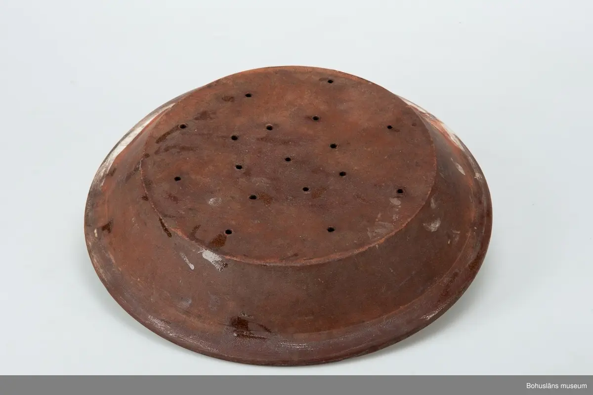 Fat med avrinningsfunktion; 17 hål om 5 mm diameter, radiellt placerade på botten. Gulglaserad insida. Uppåtböjd sida och utvikt bräm, oglaserad ut- och undersida.