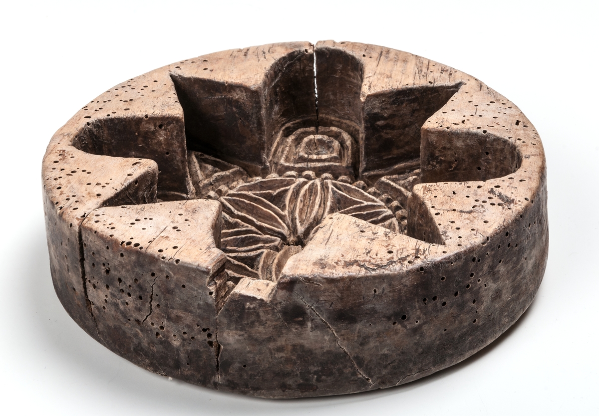 Oval ostform med skuret mönster i botten. Mitten skuren som blomma med 6 kronblad. 5 borrade genomrinningshål.
Under botten skuren märkning:
AJO 1804.
AAS
Trät har en gång i tiden angripet av trägnagare vilket lämnat efter sig riktigt med hål.