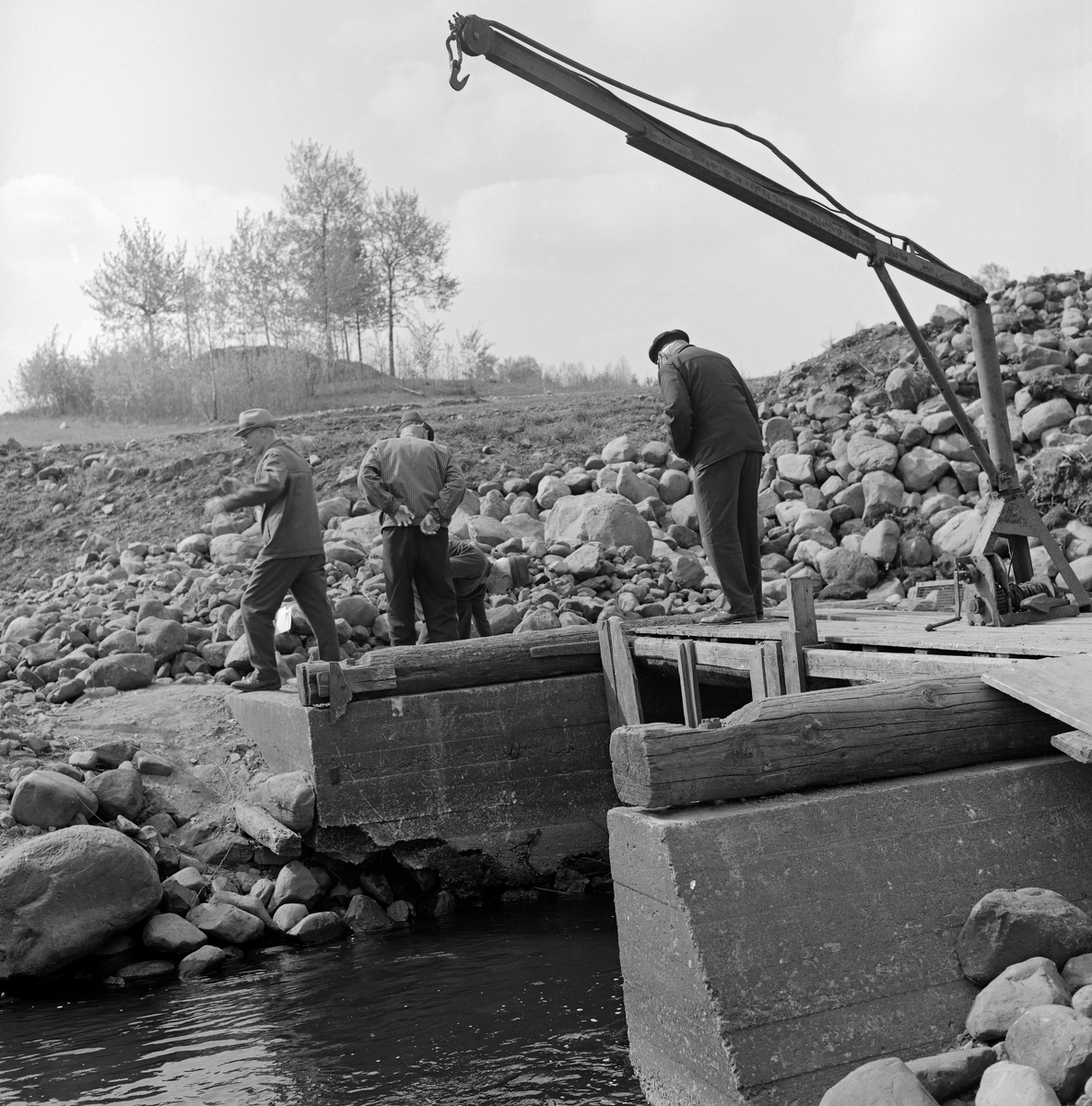 En «fiskebygning» ved Fossbakken ved Svartelva, som markerte kommunegrensa mellom Vang og Stange før vassdraget rant ut i Åkersvika og Mjøsa.  Fotografiet ble tatt i 1973.  Her hadde eierne av garden Nedre Kåterud i flere generasjoner hatt en hevdvunnen rett til å drive gytefiske – primært etter mort (Rutilus rutilus).  Vi ser at fiskebygningen var plassert i en del av elveløpet som var omgitt av støpte vanger, og der det var plass for to kuper (ruser), som ikke sto i elveløpet da dette fotografiet ble tatt.  På brua var det plassert ei kran.  På bildet ser vi (fra venstre) Birger Børresen og Martinus Hovie.  Mannen som sto på brua er foreløpig ikke identifisert.  Da dette bildet ble tatt var fiskeplassen omgitt av mye stein, antakelig fordi hovedvegen mellom Oslo og Trondheim (E6) like ved var under utvidelse.  På bakkekammen i bakgrunnen rager noe som kan se ut til å ha vært en gravhaug opp fra det omkringliggende åkerlandskapet.