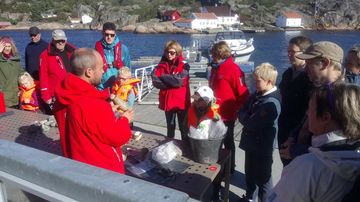Arkeolog viser frem funn fra sjøbunnen til en gruppe besøkende på brygga.
