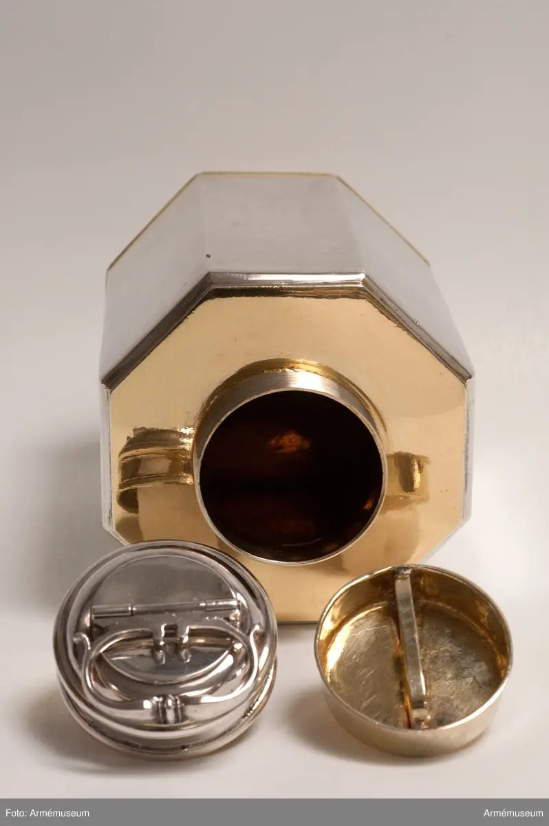 Extra förslutningslock. Locket har en plan och cirkelformad platta från vilken en 10 mm hög kant utgår. Diagonalt och fäst i kanten är ett sk. handtag. Locket är helt förgyllt.