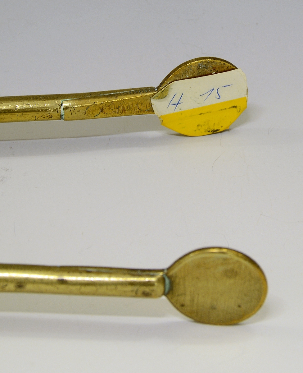 Ildtang av messing, del av peissett i tre deler. Bøyle øverst til oppheng, dreide kuler og blomst der armene deler seg. Avslutning på armene er to ovaler.